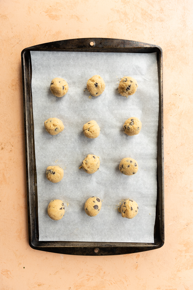 Cookie dough balls on parchment paper lined baking sheet.