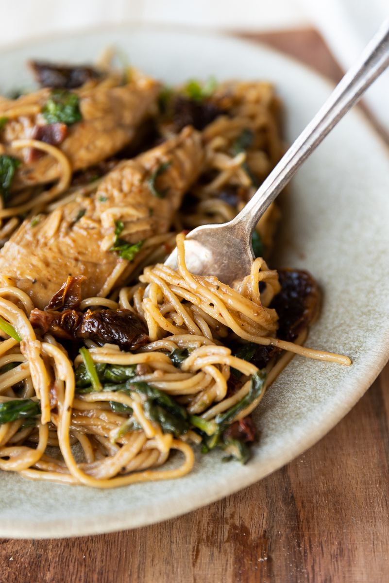 Fork twirling spaghetti on plate with Tuscan Chicken.