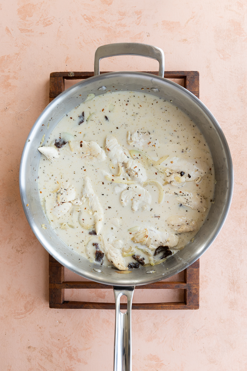 Chicken with sundried tomatoes, chicken broth, and coconut milk in pan.