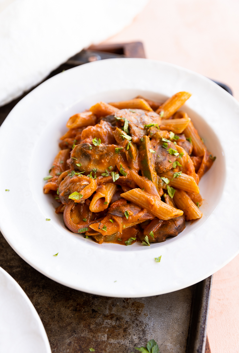 White bowl filled with penne pasta with sauce and vegetables.