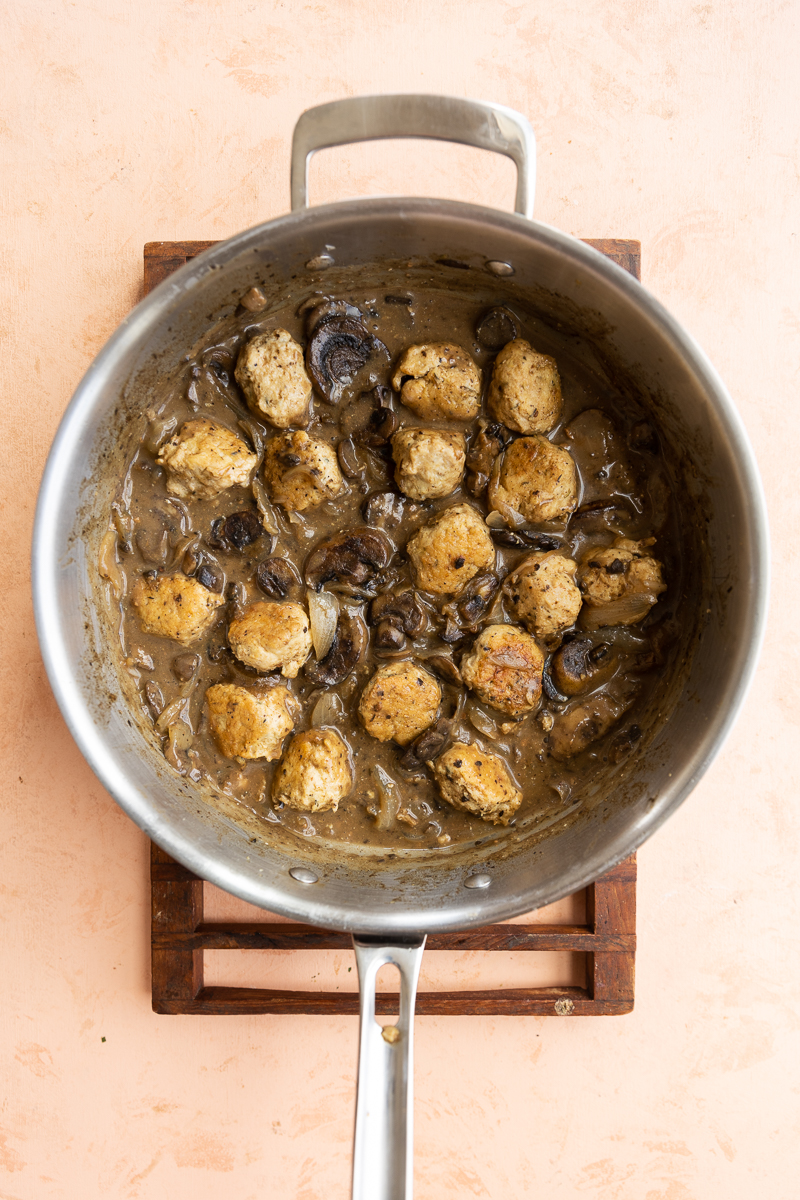 Cooked meatballs in pan with onions and mushrooms.