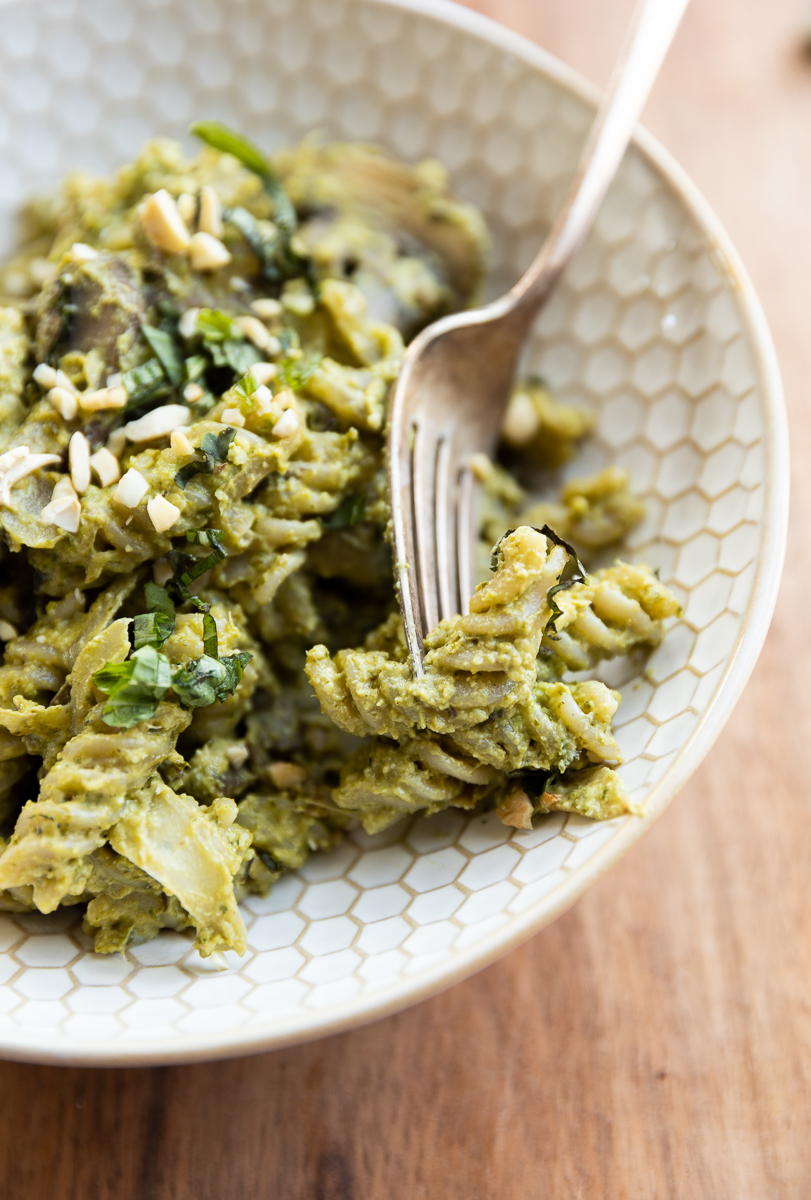 Fork scooping out pesto pasta.