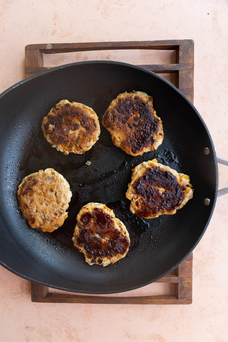 Cooked spicy chicken burgers on skillet.