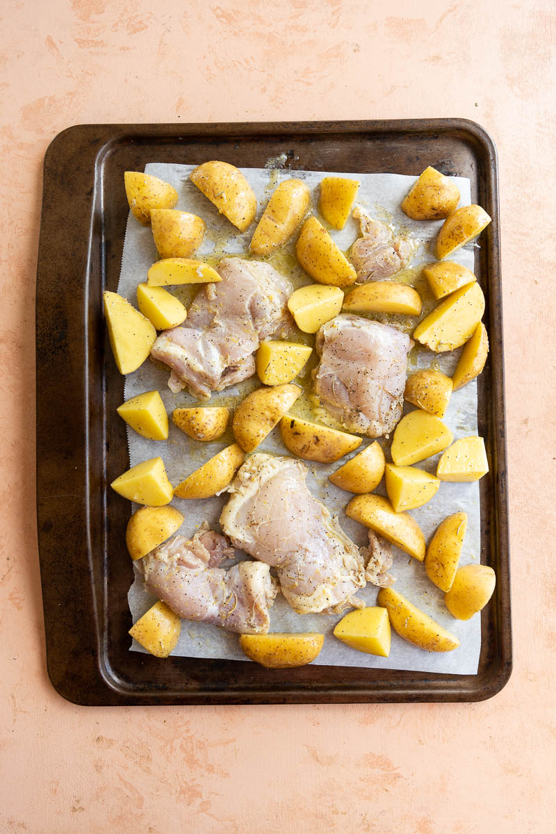 Chicken thighs and potatoes on a parchment paper lined baking sheet.