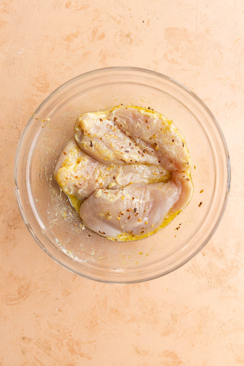Chicken marinating in glass mixing bowl.