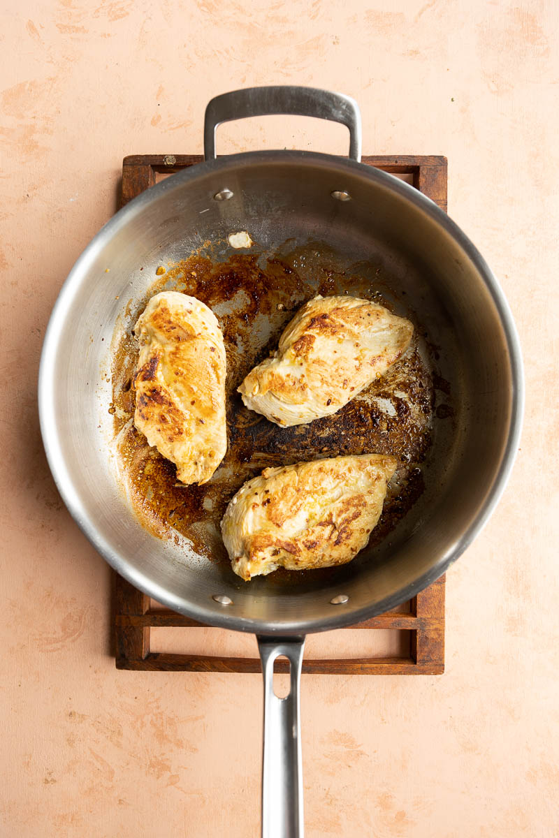 Golden brown chicken in stainless steel pan.