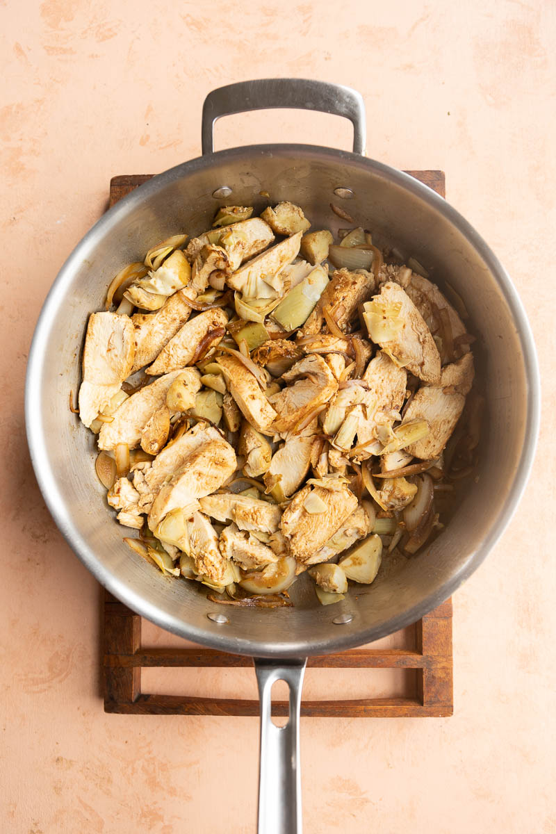 Chicken slices in stainless steel pan with artichoke hearts.