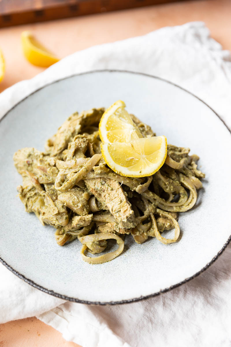 Artichoke pesto pasta with chicken on a white plate.