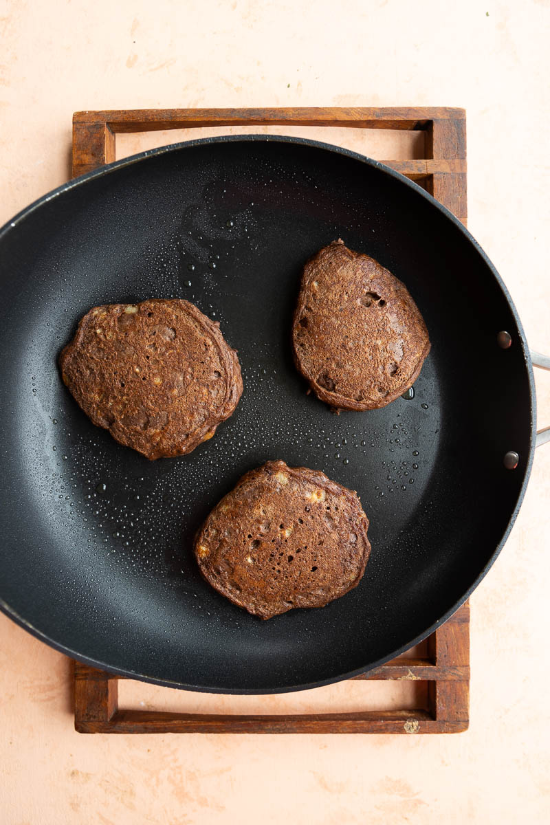 Three cooked chocolate pancakes on a frying pan.