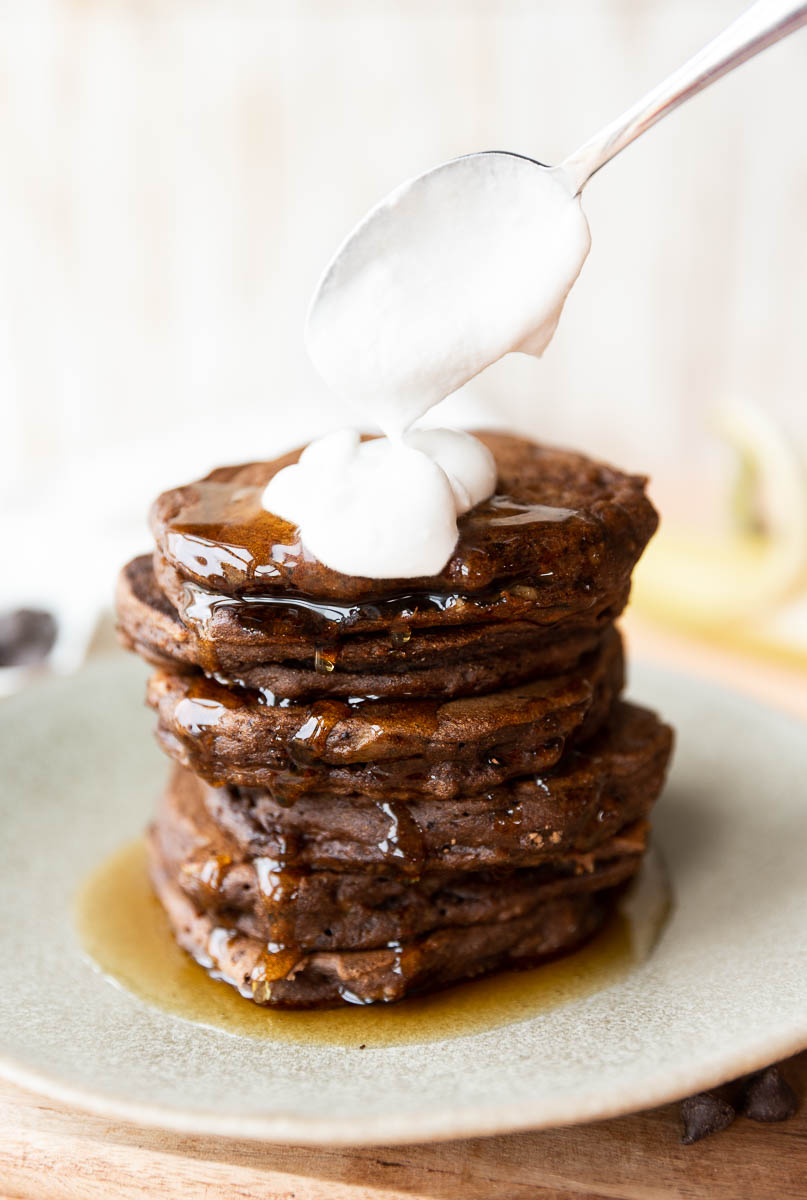 Spoon scooping coconut whipped cream onto pancake stack.