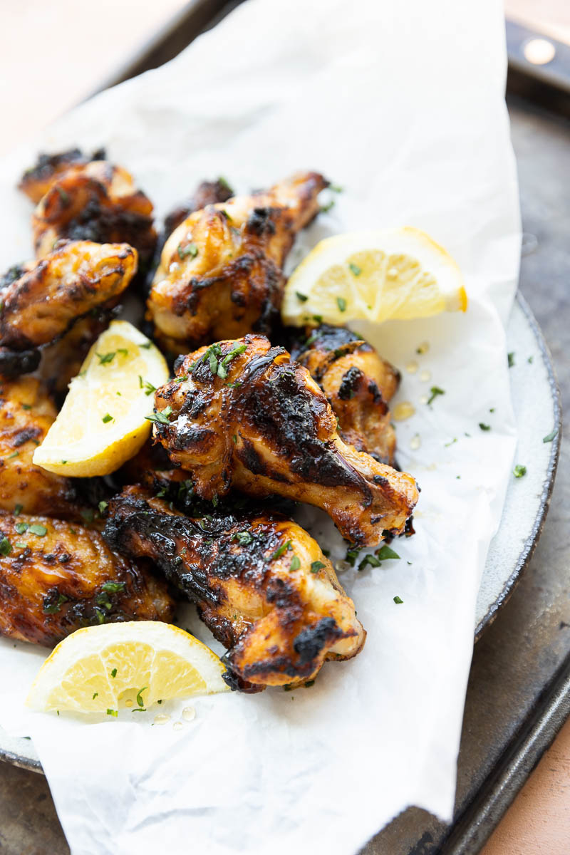 Honey lemon pepper wings on a parchment paper lined plate with fresh lemon wedges.