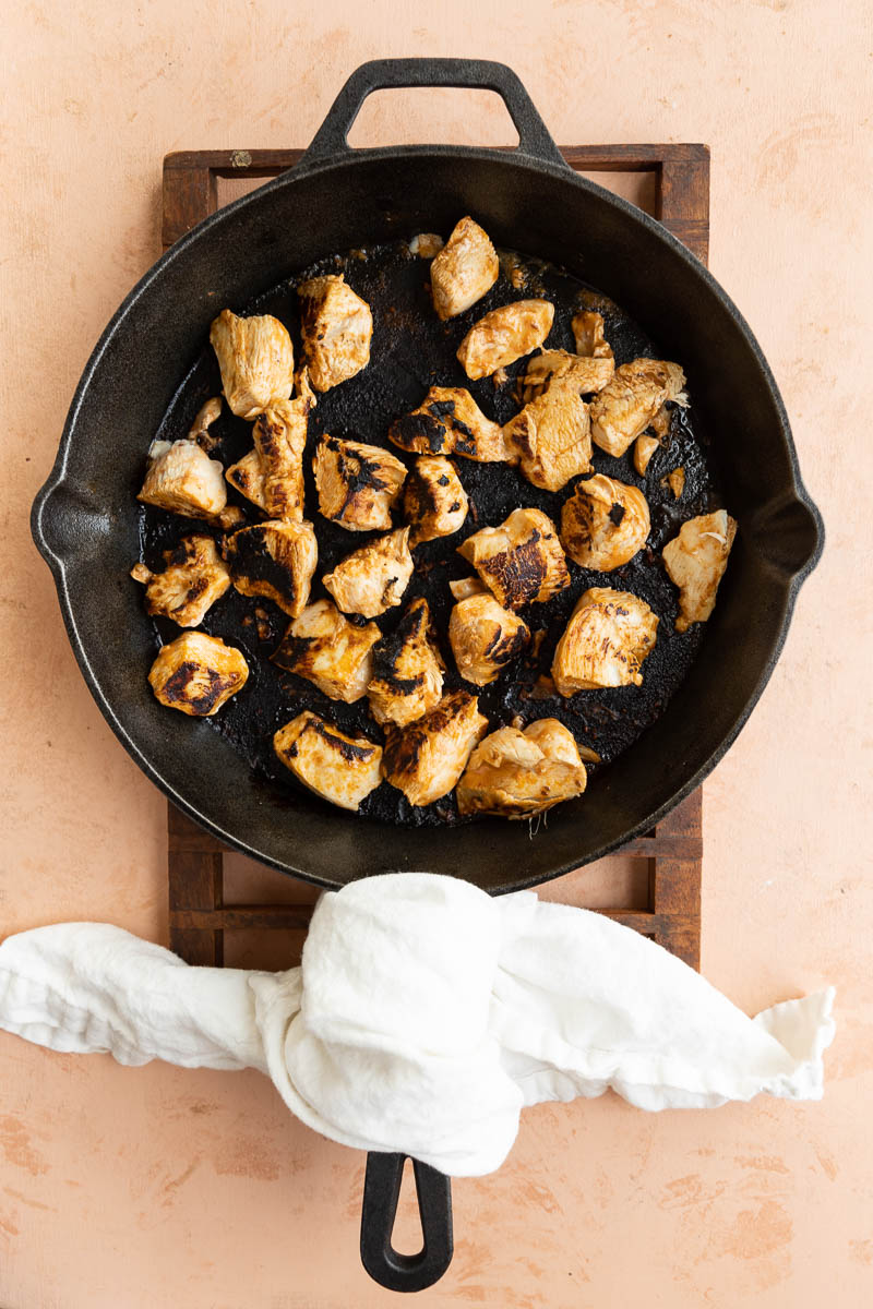 Chicken cooking on a cast iron skillet.