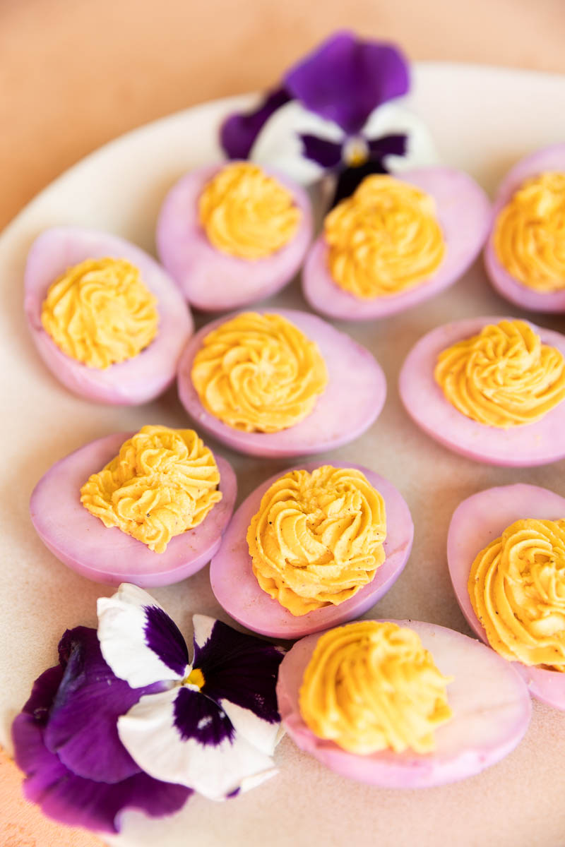 Pink deviled eggs on a cream colored plate.
