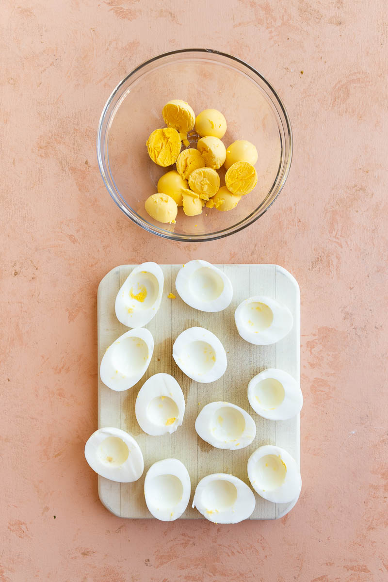 Hard boiled egg whites on a board and yolks in a mixing bowl.