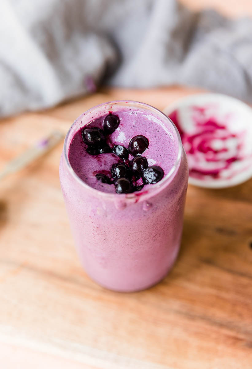 Top of blueberry protein shake in glass cup with frozen blueberries on top.