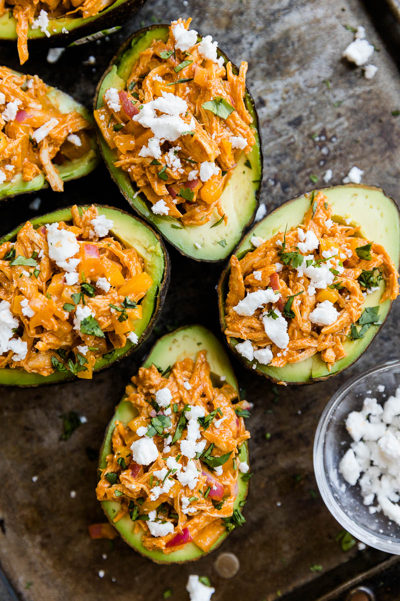 Overhead picture of stuffed avocado on a black baking tray.