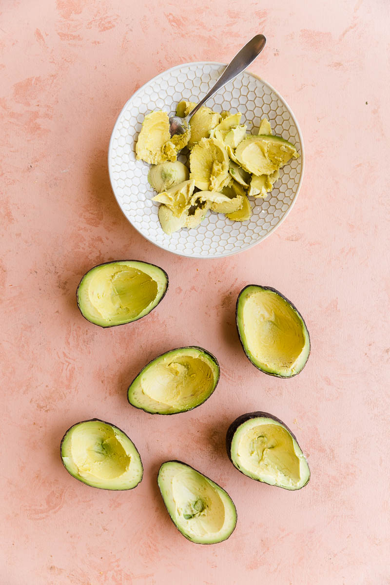 Avocado halves with some of the avocado scooped out in a bowl on the side.