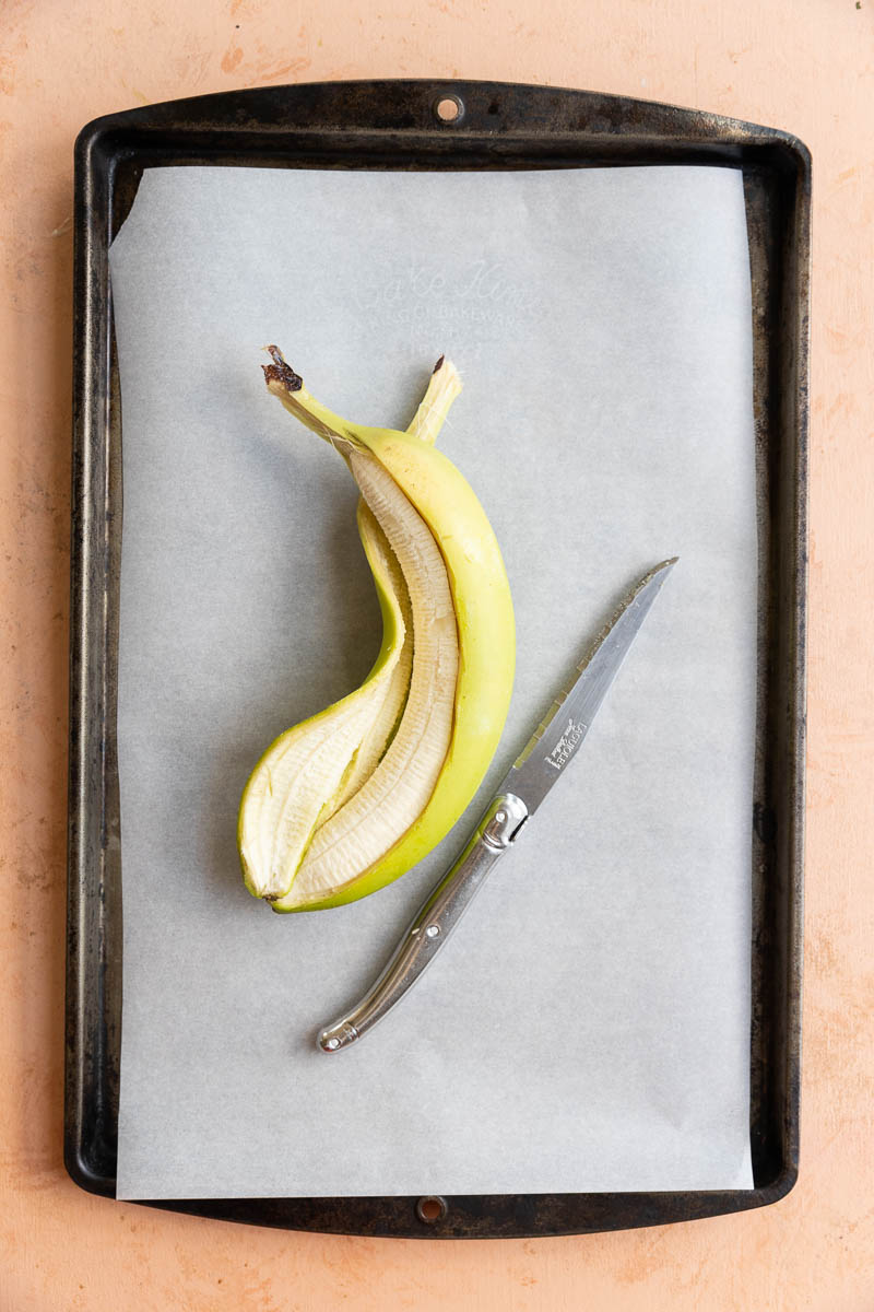 Knife and peeled banana on a baking tray lined with parchment paper.
