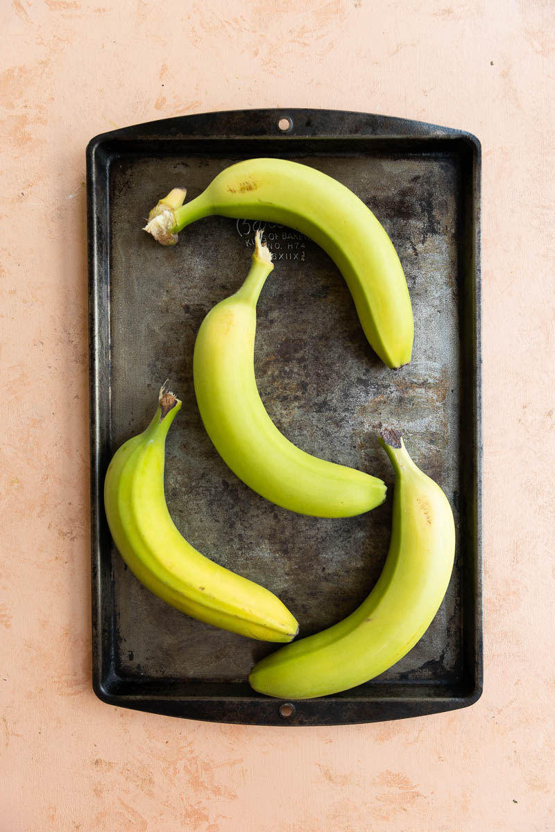 Green bananas on a baking sheet.