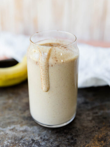 Cinnamon roll protein smoothie in a glass cup with a drip down the side.