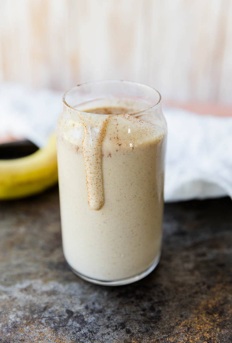 Cinnamon roll protein smoothie in a glass cup with a drip down the side.