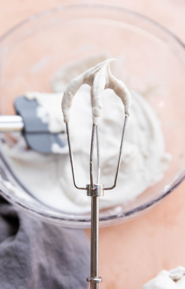 Whisk held up with fluffy whipped cream on it.
