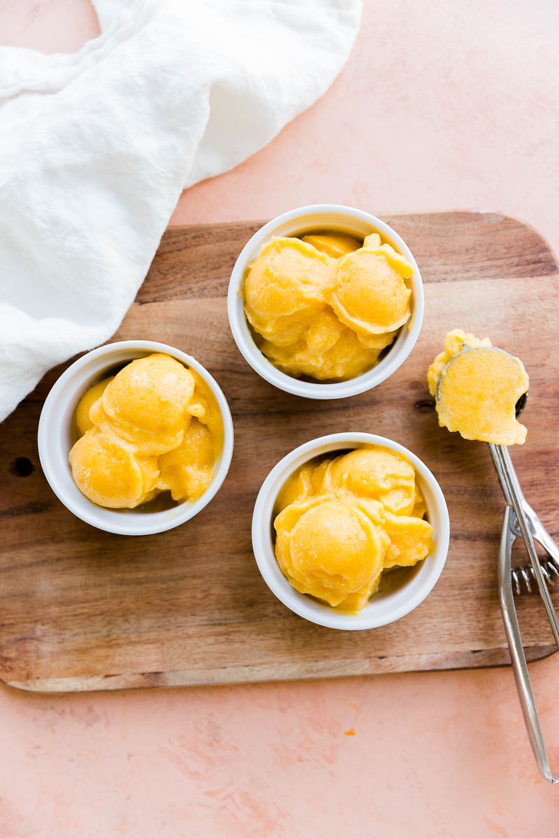 Three cups of peach sorbet with an ice cream scoop on the side.