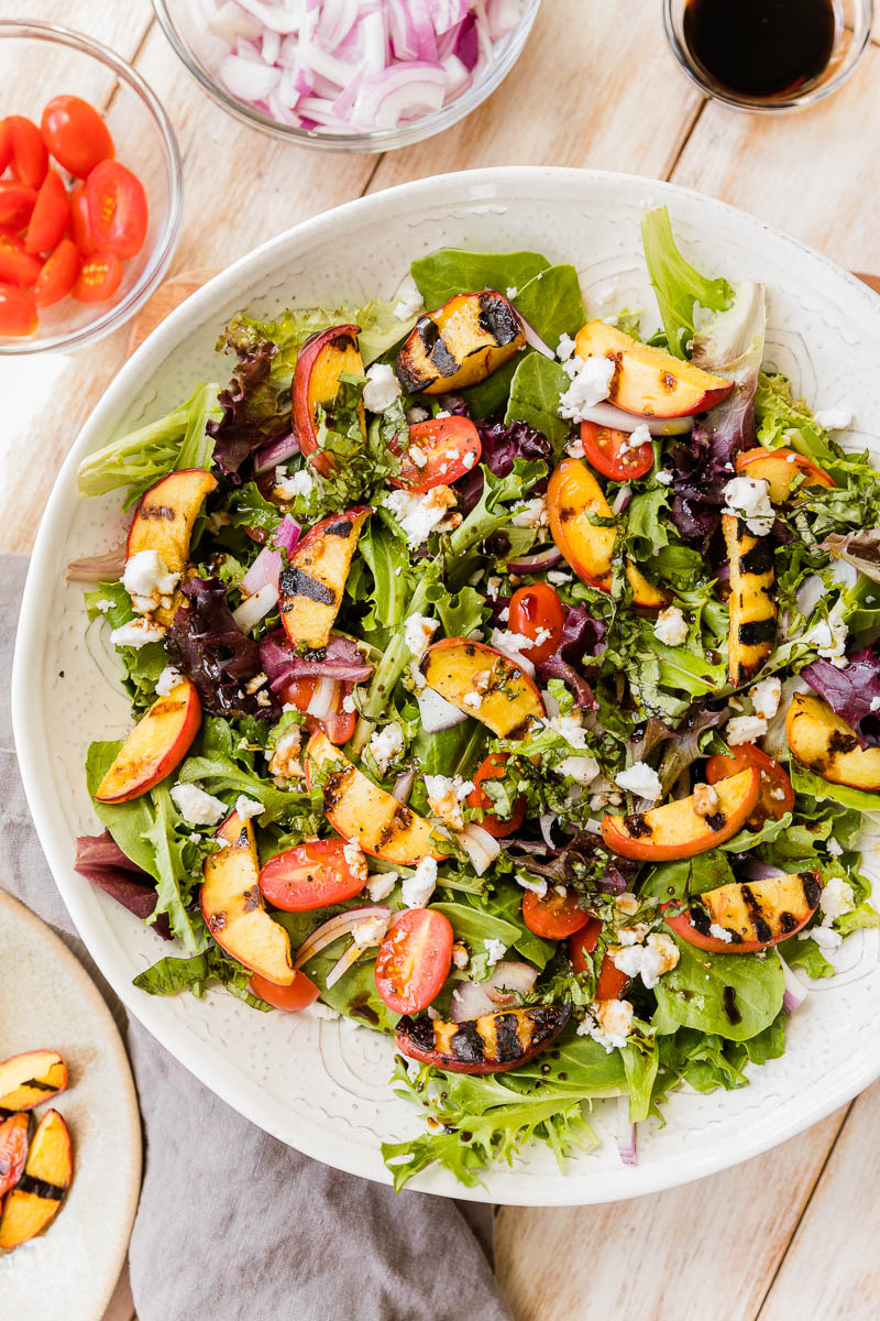 Grilled peach salad in a large white bowl.