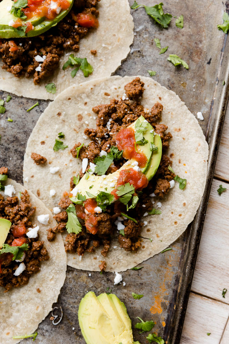 Taco with fresh avocado slices, salsa, and feta on top.
