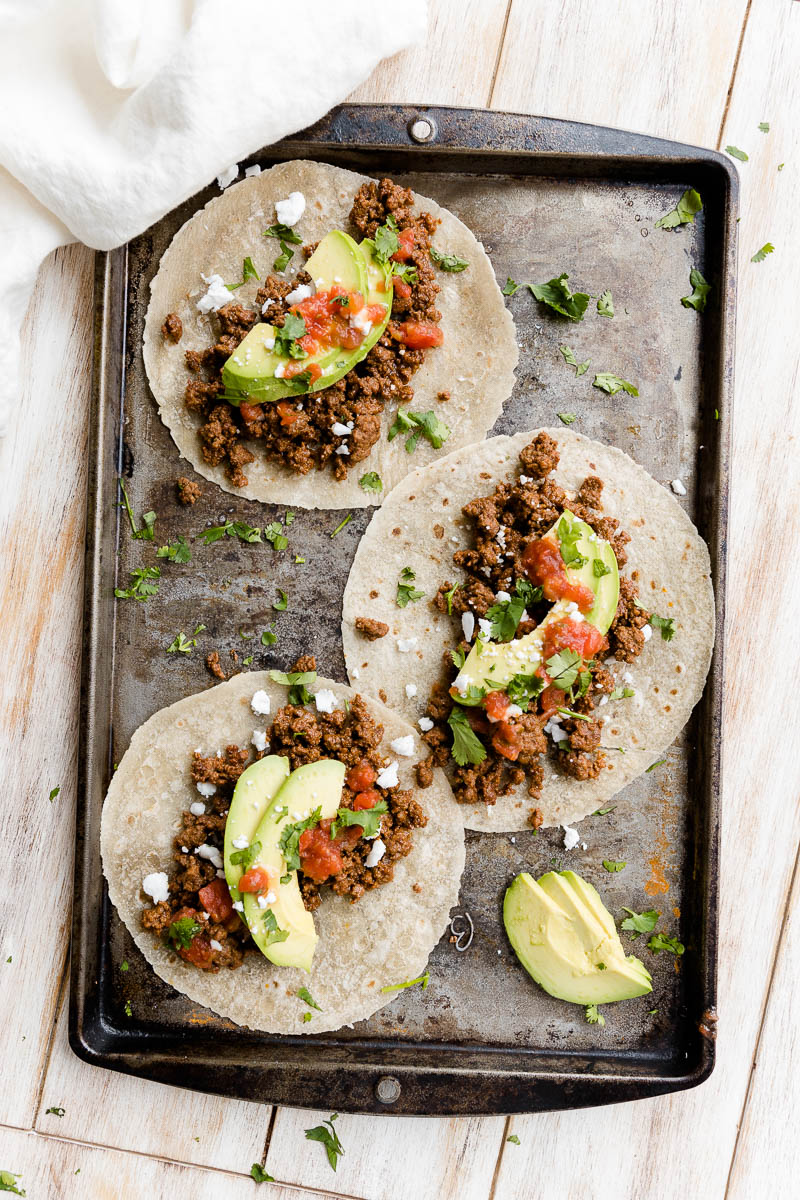 Three tacos on a black baking tray.