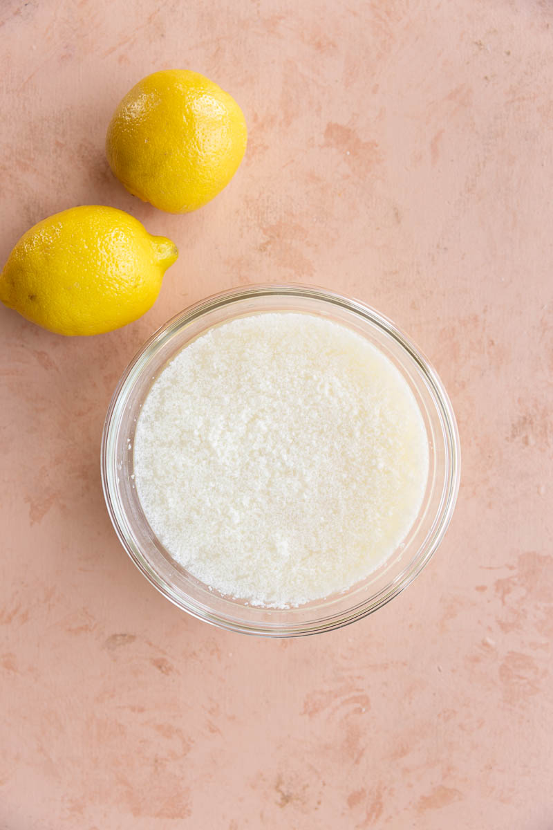 Lemon sorbet mixture in glass tupperware with lemons on the side.