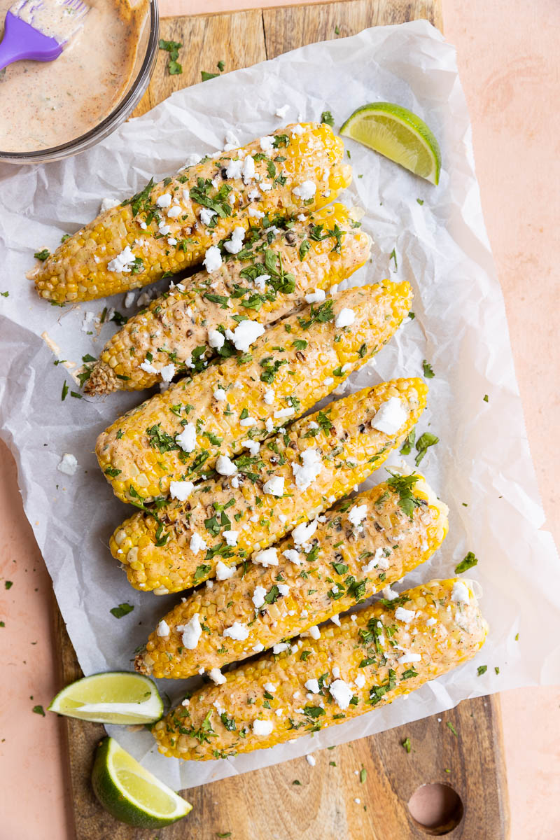 Corn topped with creamy sauce, fresh cilantro, and feta with lime wedges.