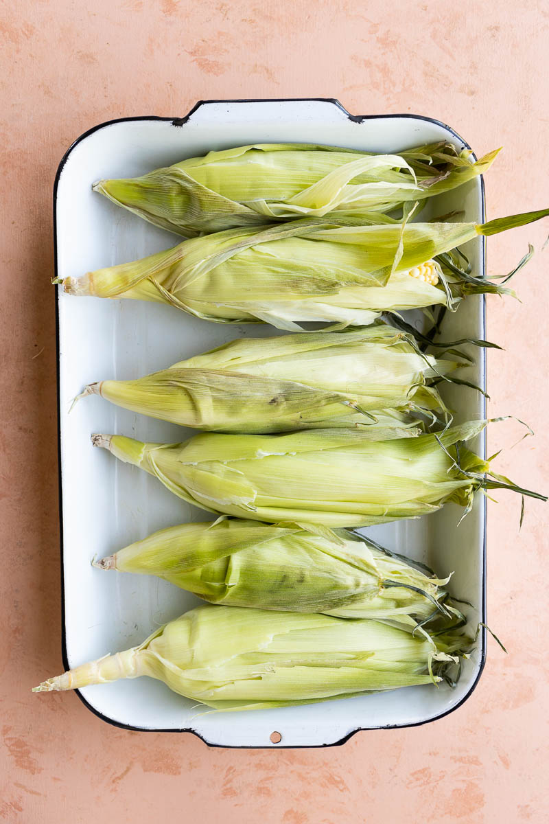 Corn soaking in a large white baking dish.