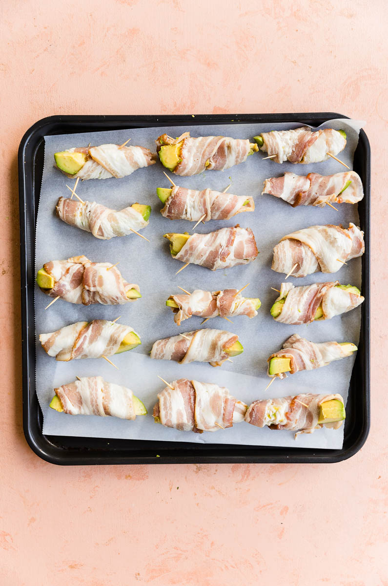 Bacon wrapped avocado wedges on a parchment paper lined baking sheet.