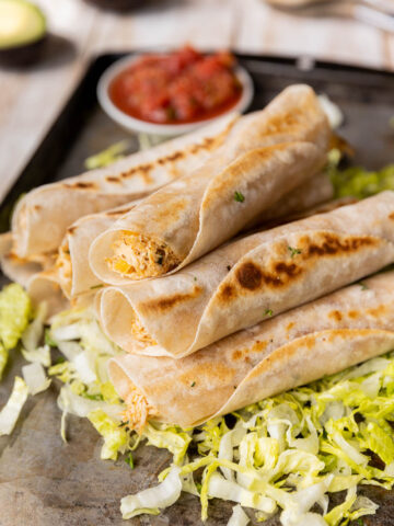 Chicken taquitos stacked up on a plate.