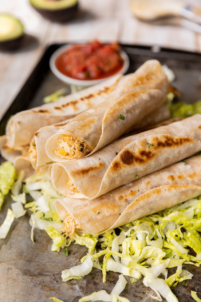 Chicken taquitos stacked up on a plate.