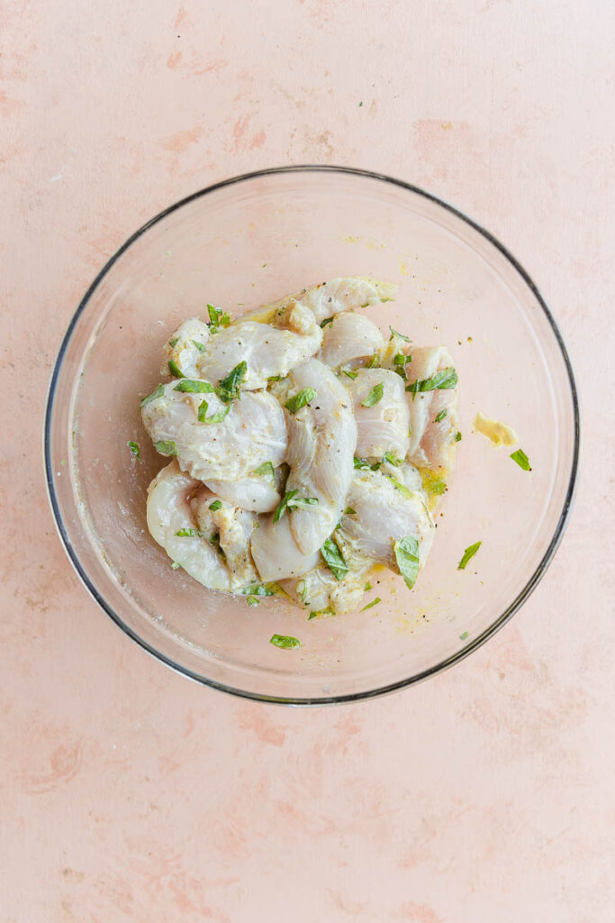 Chicken marinating in lemon juice, basil, and seasonings.