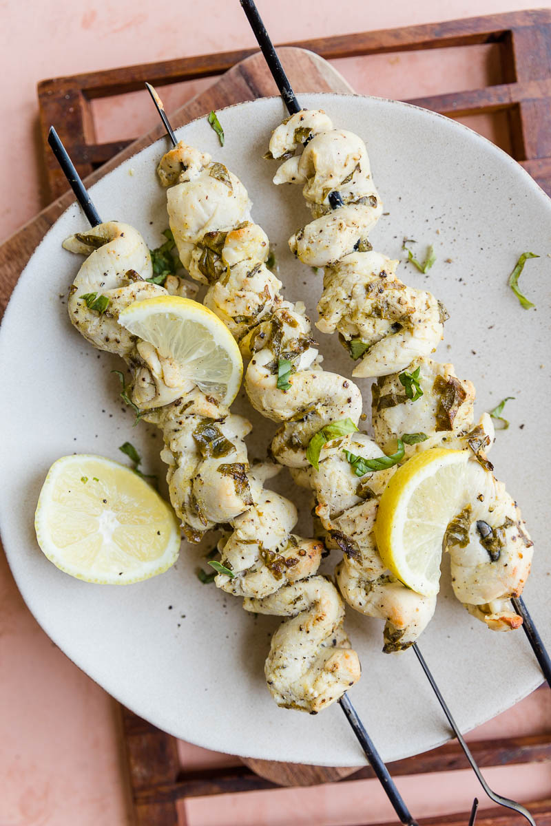 Lemon basil chicken skewers on a plate with lemon wedges.