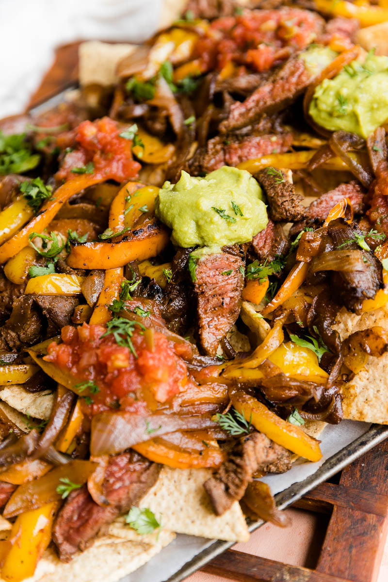 Steak fajita nachos with guacamole and salsa on top.