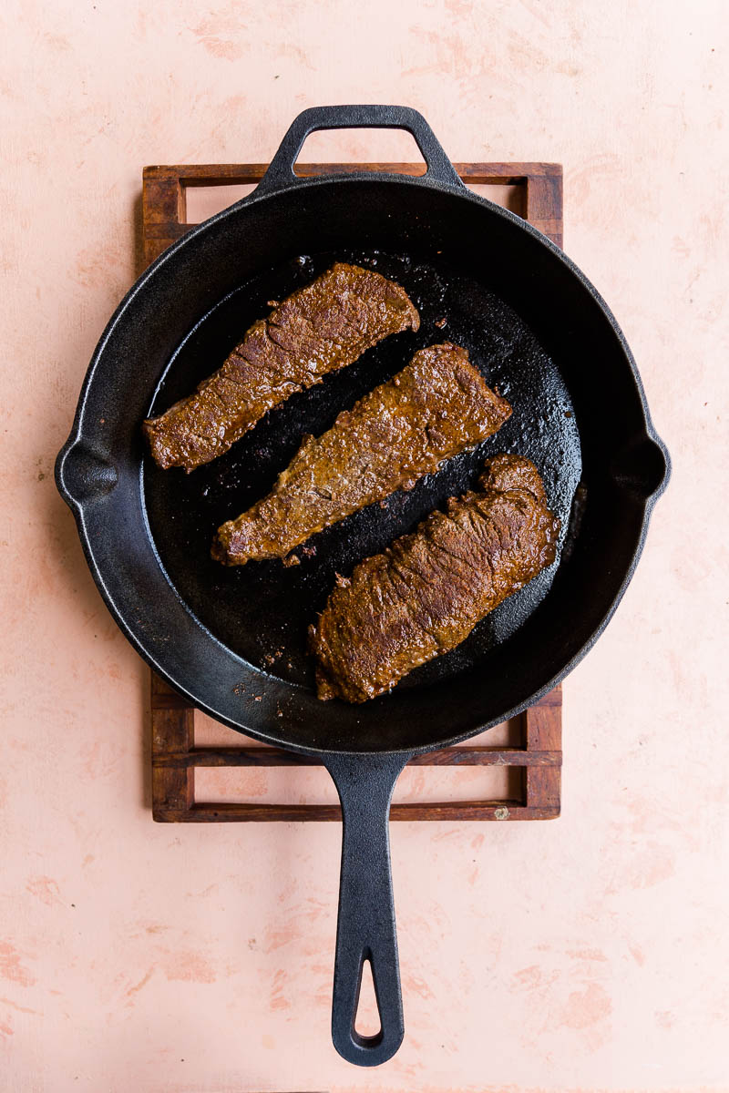 Steaks cooking in cast iron skillet.