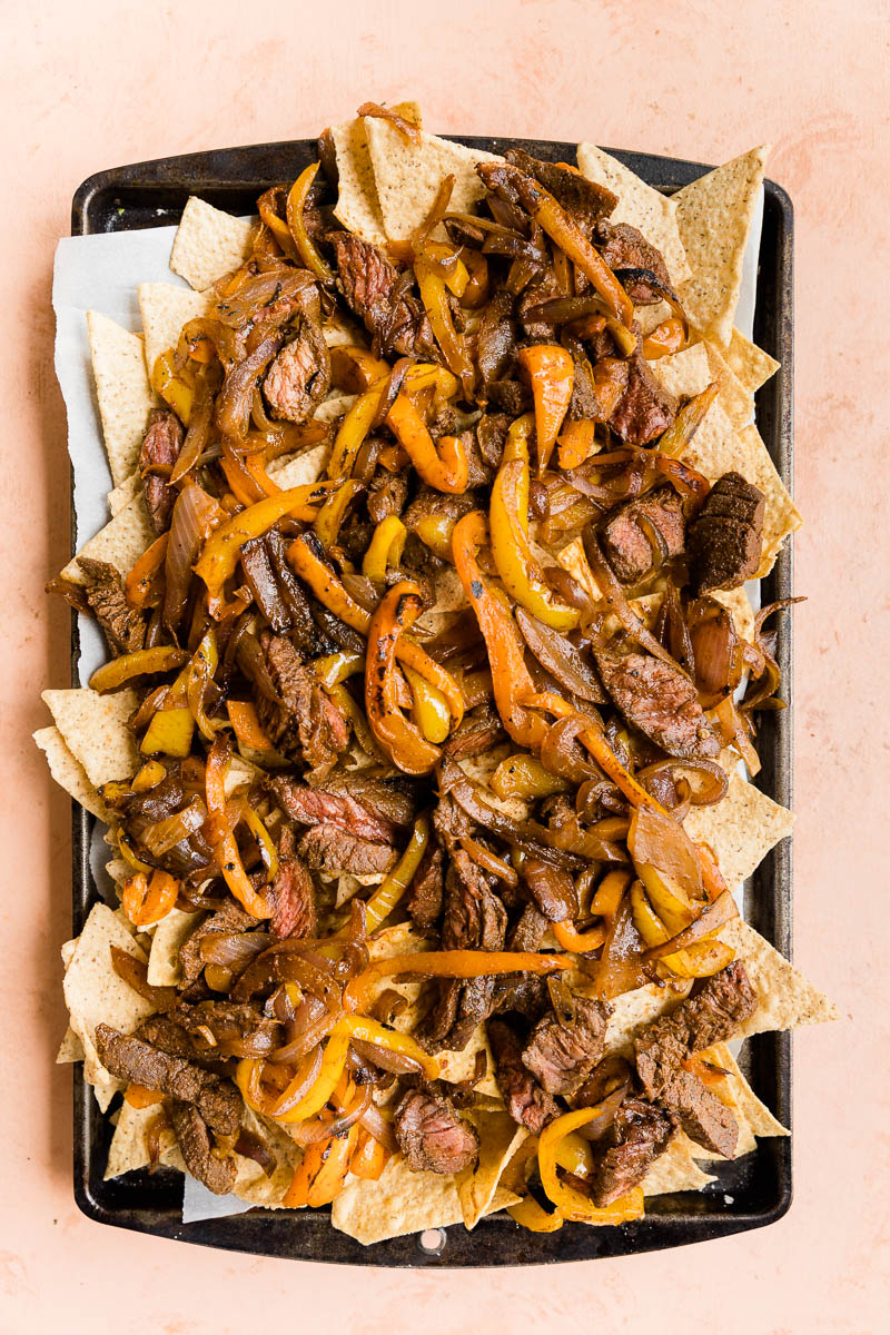 Cooked peppers and onions on top of chips on a baking sheet.