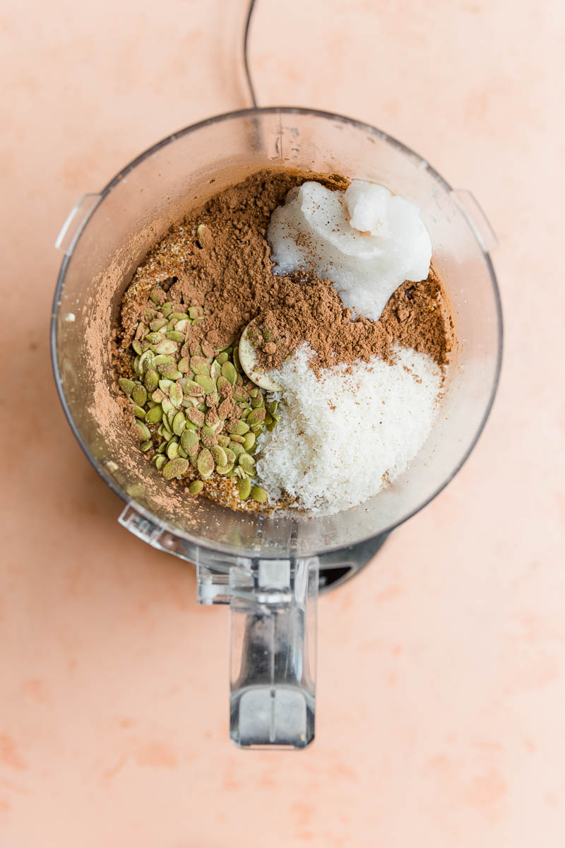 Coconut oil, cacao powder, and pumpkin seeds in food processor with almond mixture.
