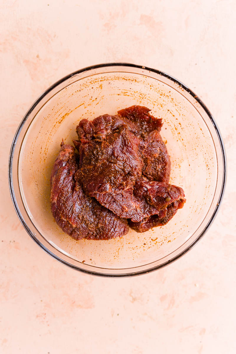 Steak marinating in glass mixing bowl.