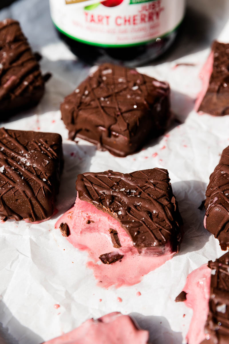 Chocolate dipped cherry ice cream bar melting on parchment paper.
