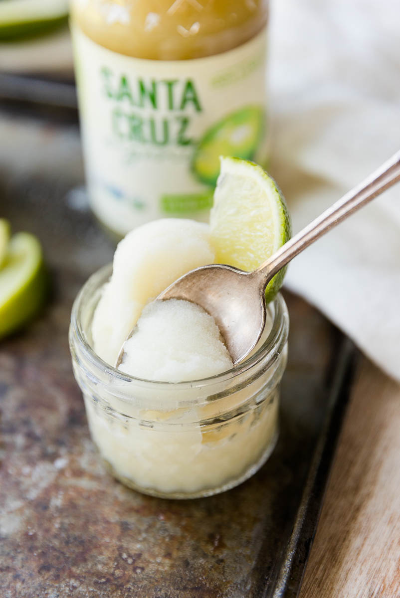 Spoon scooping out lime sorbet from small glass cup.