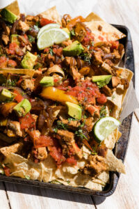 Chicken fajita nachos topped with avocado, lime wedges, and salsa.