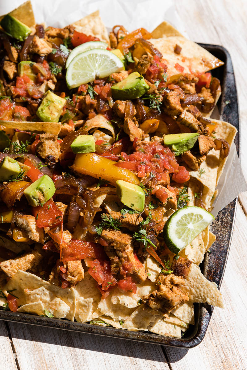 Chicken fajita nachos topped with avocado, lime wedges, and salsa.