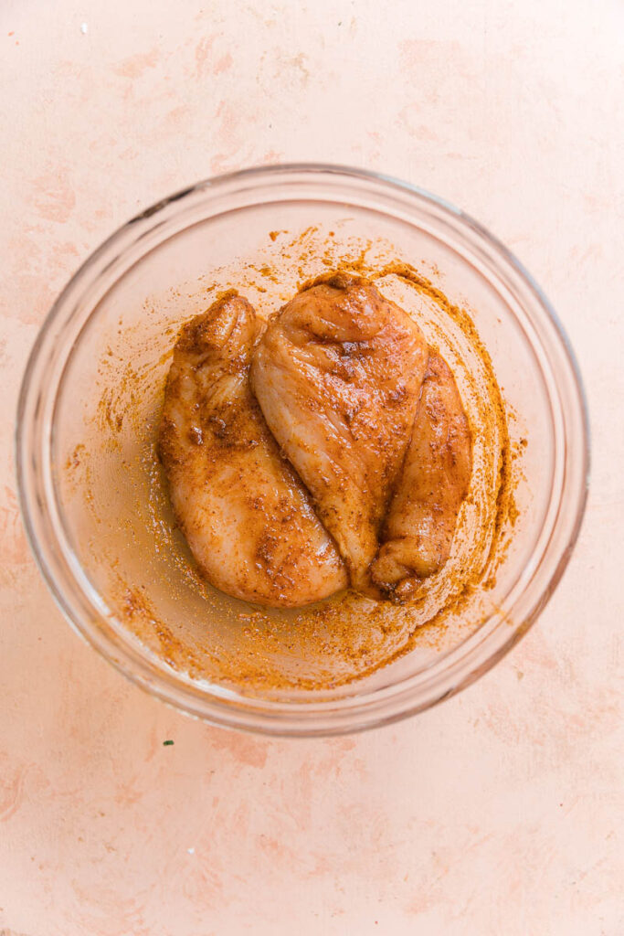 Chicken marinating in a glass bowl.