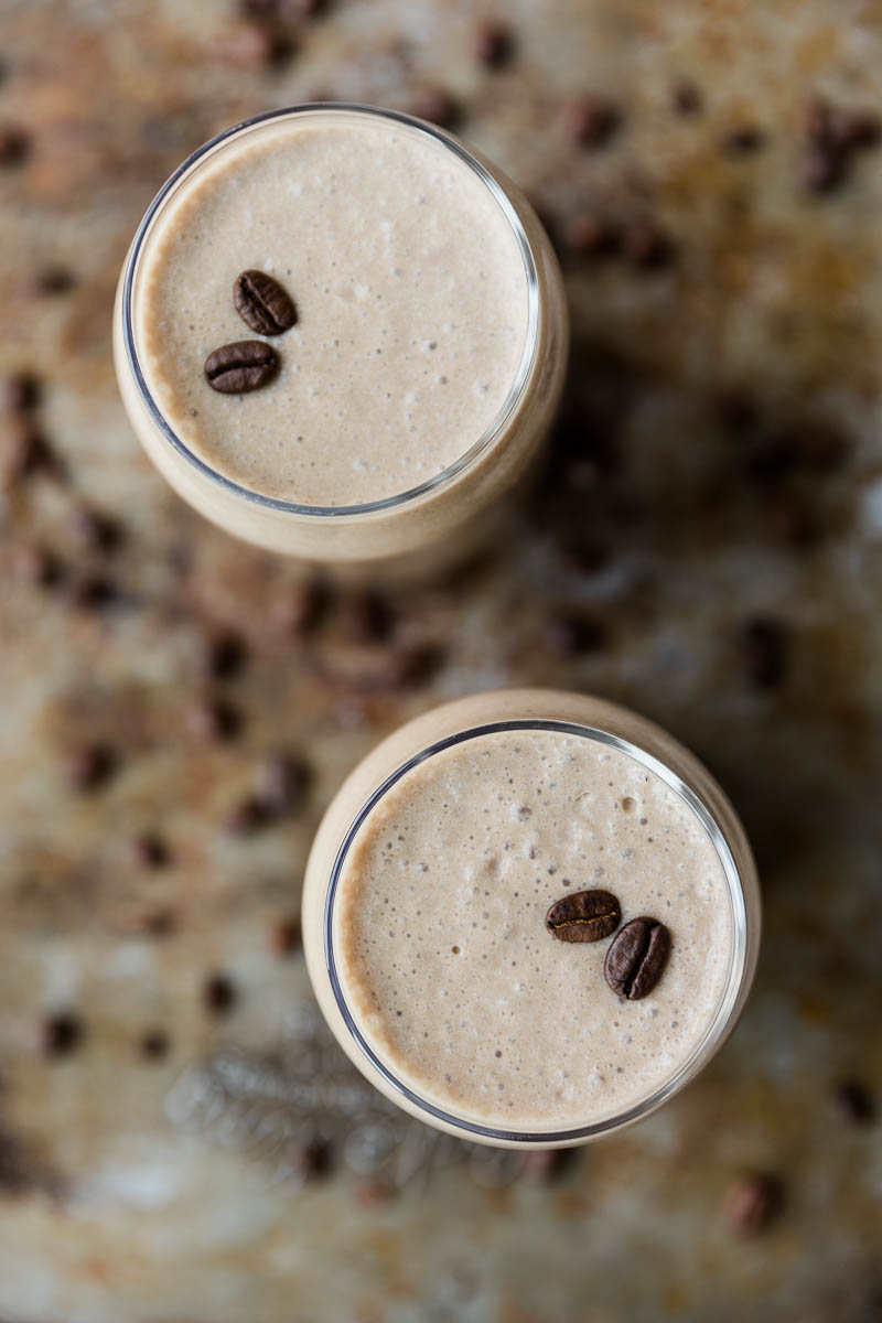 Overhead picture of coffee milkshake in two glass cups with coffee beans.