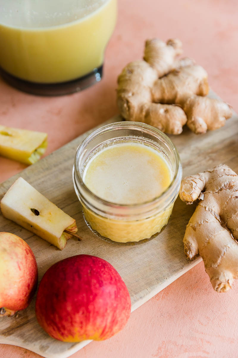 Fresh ginger shot in small glass mason jar with ginger root and apple.